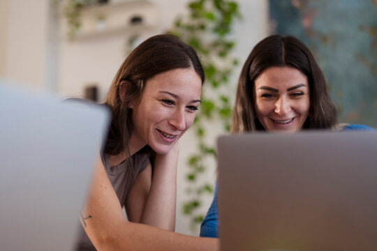 Two women are smiling while looking at a laptop screen together, sharing a moment of joy and connection.