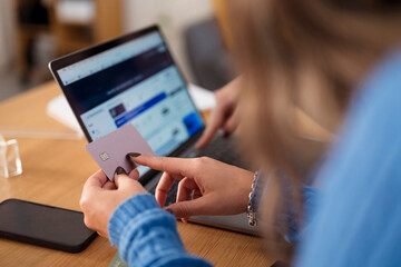 A person uses a credit card to make an online purchase on a laptop, with a smartphone nearby on the desk.