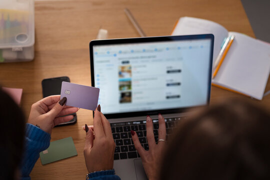 A person holds a payment card while booking a hotel online on a laptop, with another card visible on the desk.