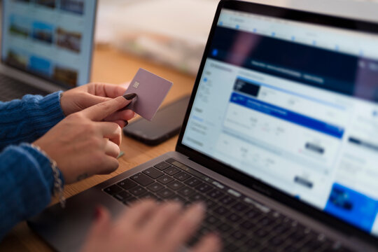 A person uses a credit card and laptop to book travel online, comparing flight prices and options for their next journey.