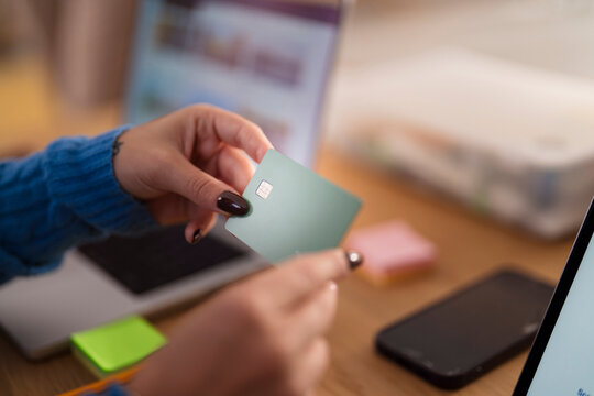 A person holds a payment card near a laptop and smartphone, suggesting online transactions or financial management.
