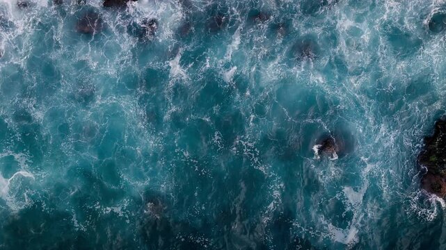 Ocean surface with white foam and dark lava reefs, aerial top down shot