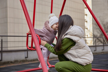 Mother pushing happy daughter on a swing set in an urban playground
