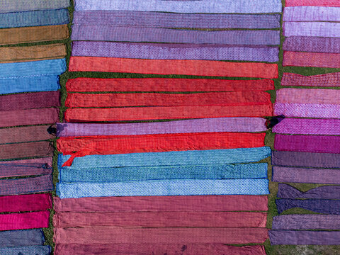 Aerial view of vibrant colored cloths laid out to dry on the grass, creating a patchwork of textures and hues, Narayanganj, Dhaka Division, Bangladesh.