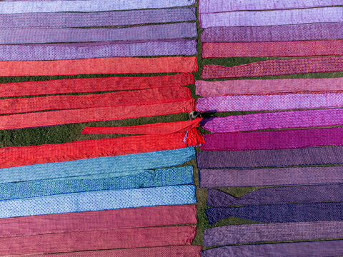 Aerial view of vibrant, colorful textiles laid out in neat rows on a green field, creating a striking contrast of textures and hues, Narayanganj, Dhaka Division, Bangladesh.