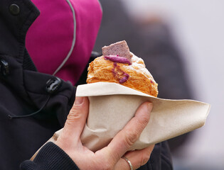 A close-up of a womans hand holding a freshly bought muffin wrapped in a napkin at an Naplavka outdoor farmers market in Prague.