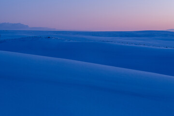 Silhouettes of snowy fields dyed deep blue before dawn