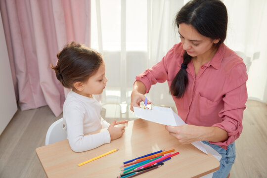 Mother and daughter cutting designs from paper with scissors for an art project