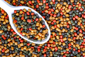 Dry food for aquarium fish on  spoon compound fish feed flakes.Pile of flakes and granules for feeding tropical aquarium fishTop view.Aquarium