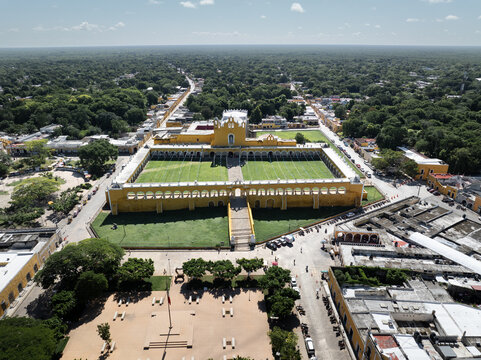 Aerial view of the vibrant yellow Convent of San Antonio de Padua contrasts with the deep green grass and surrounding lush trees, Izamal, Yucatan, Mexico.