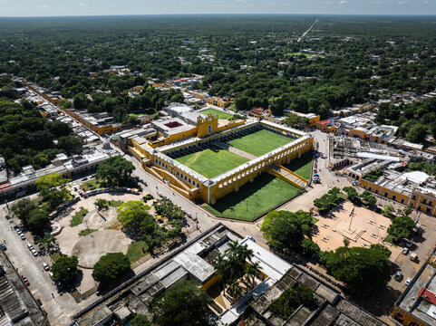 Aerial view of the vibrant yellow Convent of San Antonio de Padua standing out against the lush green canopy, a striking contrast of color and history, Izamal, Yucatan, Mexico.
