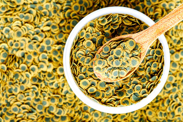 Dry food for aquarium fish on a wooden spoon compound fish feed flakes.Pile of flakes and granules for feeding tropical aquarium fishTop view.Aquarium
