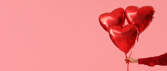 Female hand with air balloons in shape of heart on pink background. Valentine's Day celebration © Pixel-Shot