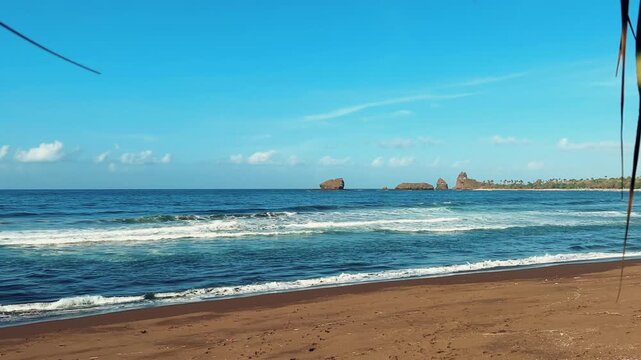 The sea in Jember, East Java. Indonesia. Watu Ulo beach with dark sand, mountains and coral rocks towering above the beach. The raging blue Indian ocean on a sunny day. 4К