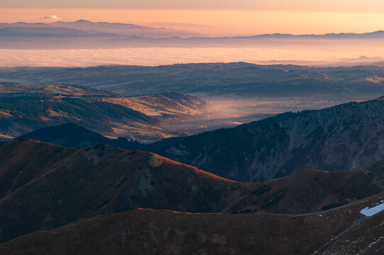 Aerial view of the undulating, shadowy mountain ridges fading into a misty valley under a soft, glowing sky, Pribylina, Zilina Region, Slovakia.