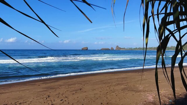 The sea in Jember, East Java. Indonesia. Watu Ulo beach with dark sand, mountains and coral rocks towering above the beach. The raging blue Indian ocean on a sunny day. 4К