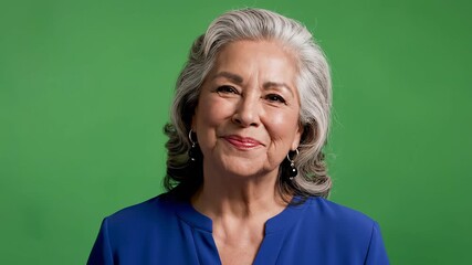 Portrait of a cheerful senior Hispanic woman with gray hair smiling brightly against a vibrant green background exuding warmth and positivity in a studio setting. - Powered by Adobe