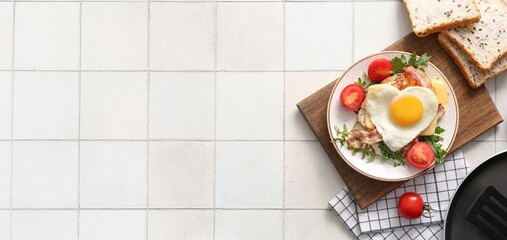 Plate with tasty heart-shaped fried egg, bacon, toasts, tomatoes and arugula on light tile...