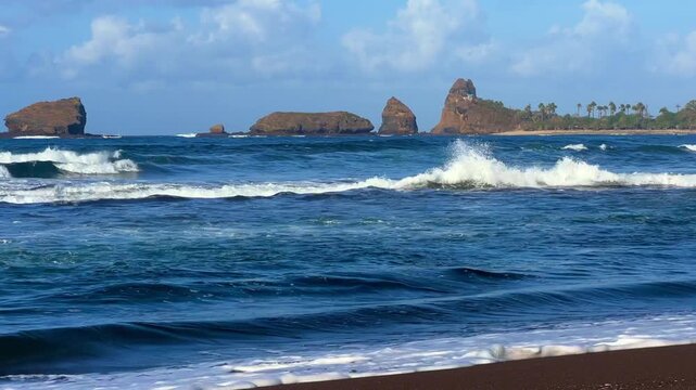 The sea in Jember, East Java. Indonesia. Watu Ulo beach with dark sand, mountains and coral rocks towering above the beach. The raging blue Indian ocean on a sunny day. 4К	