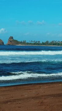The sea in Jember, East Java. Indonesia. Watu Ulo beach with dark sand, mountains and coral rocks towering above the beach. The raging blue Indian ocean on a sunny day. 4К