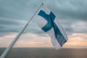 Finland flag flying over Baltic Sea at sunset