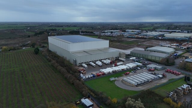 Aerial view of a vast distribution center with rows of parked trucks under a muted, overcast sky, Wisbech, England, United Kingdom.