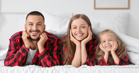 Happy parents with their little daughter lying under blanket in bedroom