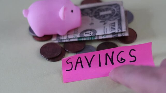Un primer plano de un cerdo de color rosado con una nota con la palabra ahorros y rodeado de dinero en un fondo de color amarillo claro