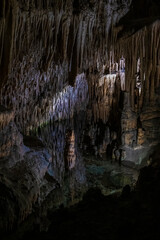 Mystical underground cave illuminated by soft artificial light, showcasing dramatic stalactites, rock formations, and reflections over a still subterranean lake