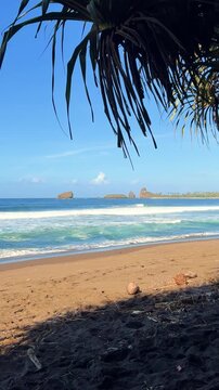 The sea in Jember, East Java. Indonesia. Watu Ulo beach with dark sand, mountains and coral rocks towering above the beach. The raging blue Indian ocean on a sunny day. 4К