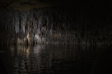 Fototapeta premium Mystical underground cave illuminated by soft artificial light, showcasing dramatic stalactites, rock formations, and reflections over a still subterranean lake