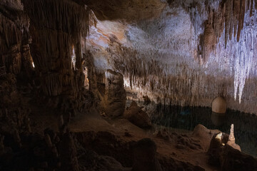 Mystical underground cave illuminated by soft artificial light, showcasing dramatic stalactites, rock formations, and reflections over a still subterranean lake