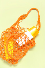 Naklejka premium Mesh bag with bottles of sunscreen cream on beige background
