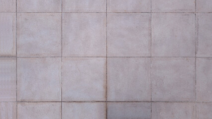 Light gray outdoor tile floor made of composite material with rough, striated, and linear texture. Grey square exterior tiles with wear and dirt in grout lines. Industrial, pavement, urban style. 