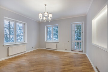 Bright and spacious room features wooden flooring and large windows showcasing a winter landscape outside. Warm lighting enhances the inviting atmosphere