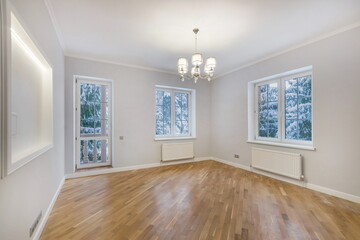 This room features large windows allowing natural light, with snow visible outside. The wooden floor and chandelier create a warm, inviting atmosphere perfect for various uses