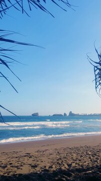 The sea in Jember, East Java. Indonesia. Watu Ulo beach with dark sand, mountains and coral rocks towering above the beach. The raging blue Indian ocean on a sunny day. 4К
