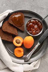 Plate with bowl of sweet apricot jam  and toasts on grey background