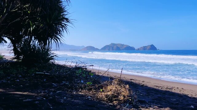The sea in Jember, East Java. Indonesia. Watu Ulo beach with dark sand, mountains and coral rocks towering above the beach. The raging blue Indian ocean on a sunny day. 4К