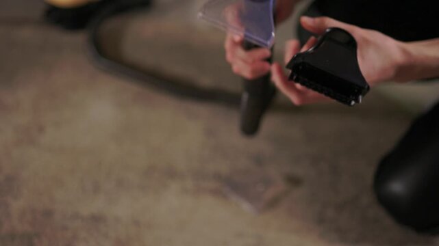 Person connecting vacuum nozzle to equipment near carpet surface, Individual kneeling and adjusting vacuum attachment on carpet with background lighting and equipment