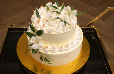 Wedding cake, a cream cake decorated with cream and flowers on a gold tray.