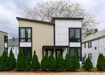 Modern two-story duplex with bold geometric facade and evergreen hedge in Brighton, Boston, Massachusetts, USA
