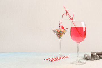 Glass of tasty cocktail with straw and bartender tools on blue grunge table against white background. Valentine's Day celebration