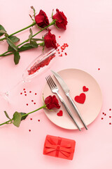 Beautiful table setting with red roses, gift box and hearts on pink background. Valentine's Day celebration