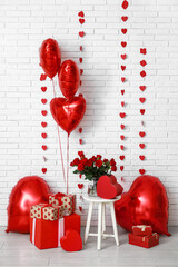 Heart shaped air balloons with gift boxes and bouquet of red roses near white brick wall....