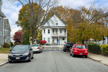 A quiet residential street leading to a white family home framed by vibrant autumn trees in Brighton, Boston, Massachusetts, USA
