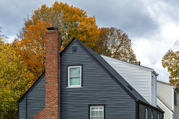 Classic architectural style of a suburban home with dark grey siding and red brick chimney in the Brighton area of Boston, Massachusetts, USA
