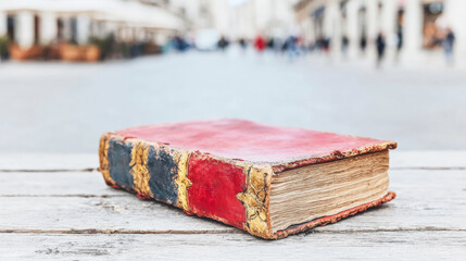 Old worn book with a red leather cover and gilded spine, resting on a white wooden surface, bringing a sense of heritage