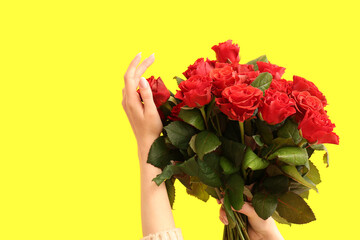 Female hands with bouquet of beautiful red roses on yellow background. Valentine's day celebration