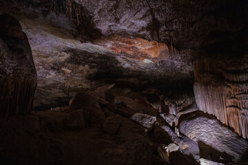Large underground chamber filled with dense stalactites and rock formations, illuminated by soft artificial light inside a deep limestone cave